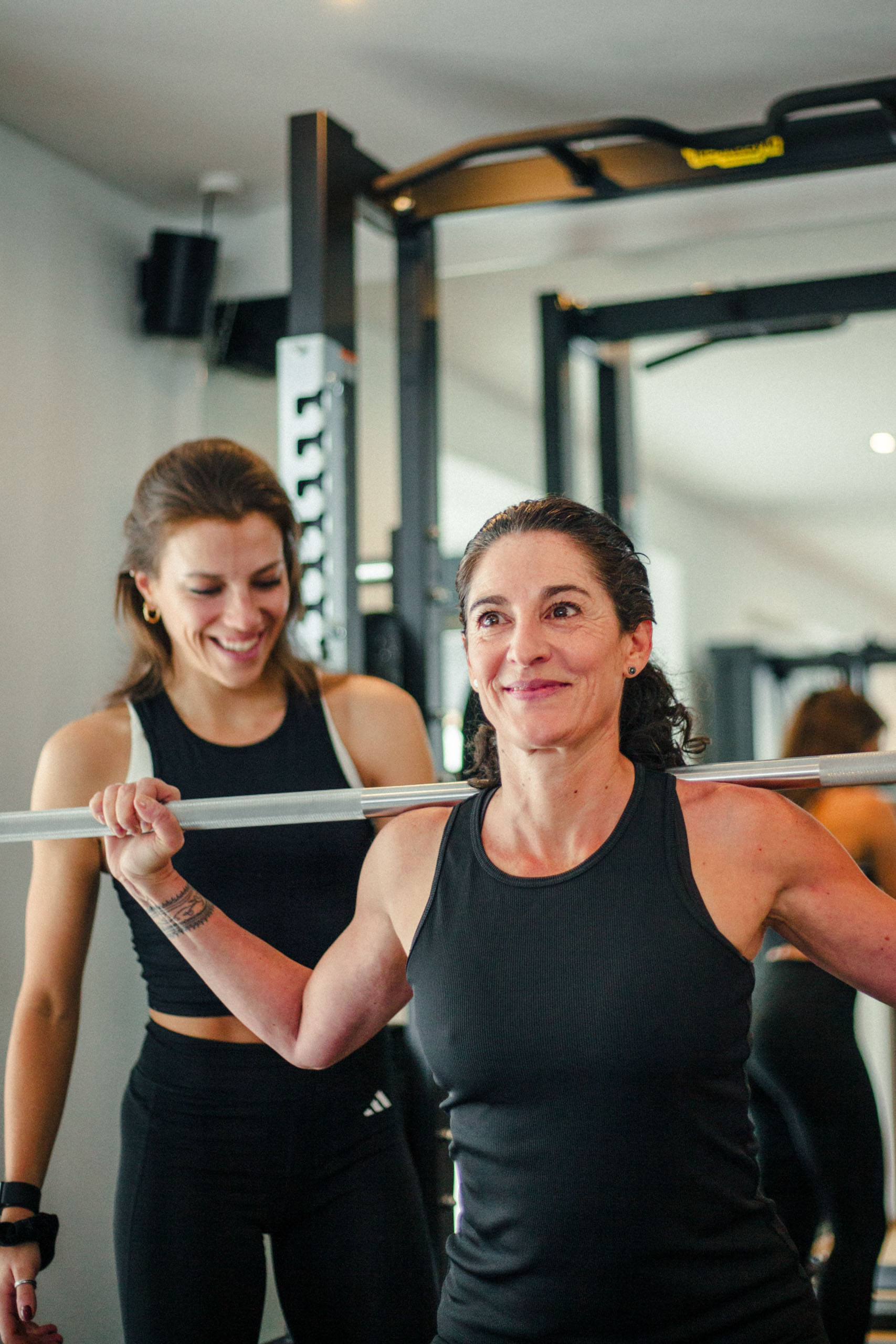 Trainerin unterstützt eine Sportlerin bei einer Übung mit einer Langhantel