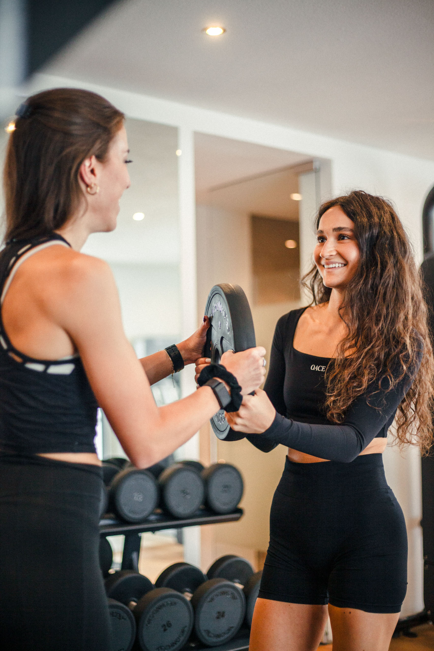 Trainerin unterstützt eine Sportlerin beim korrekten Ausführen der Übung mit einer Gewichtsscheibe
