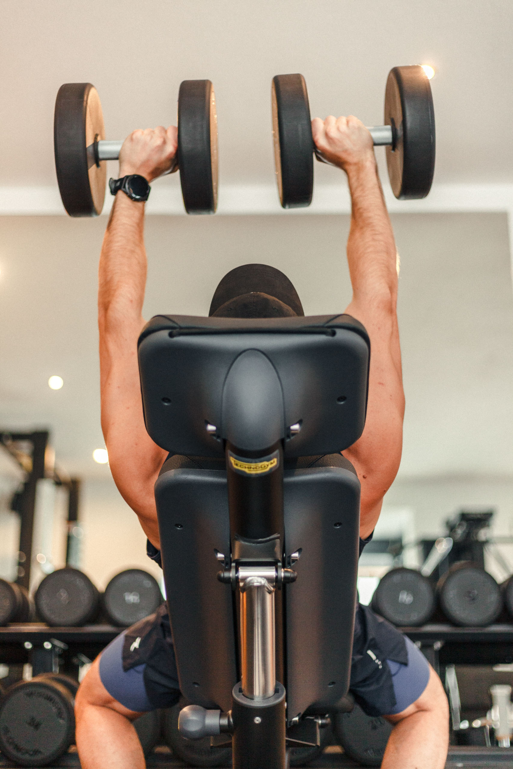 Sportler beim Bankdrücken mit Kurzhanteln am Rack
