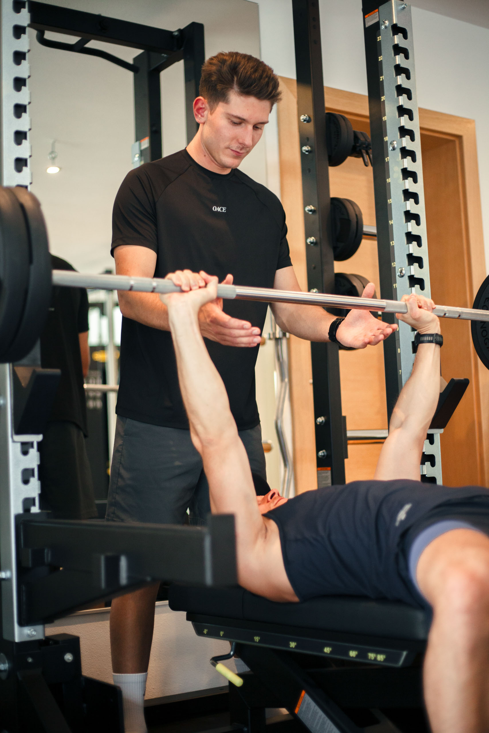 Trainer unterstützt einen Sportler beim korrekten Bankdrücken am Rack